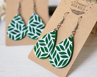 Puede incluir: Un par de pendientes de color verde y blanco en forma de lágrima con un patrón de hojas. Los pendientes están en una tarjeta marrón con el texto "Run Wild" impreso en ella.
