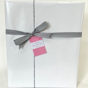 May include: A wrapped gift with white paper, tied with a black and white chevron ribbon and twine. A pink polka dot tag reads "Happy Mother's Day Mom!" in black script. The gift is ready for a special occasion.