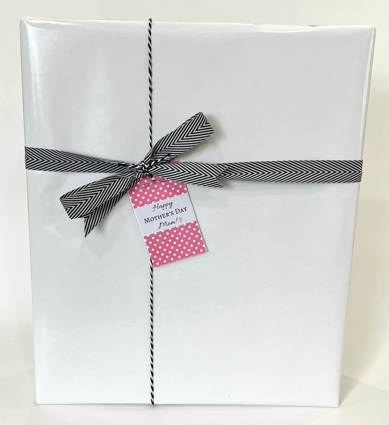 May include: A wrapped gift with white paper, tied with a black and white chevron ribbon and twine. A pink polka dot tag reads "Happy Mother's Day Mom!" in black script. The gift is ready for a special occasion.