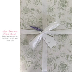 May include: A gift wrapped in sage green and white floral paper, tied with a white satin ribbon. A small tag is attached, and a faux floral sprig adds a decorative touch. The gift wrap features a repeating pattern of flowers.