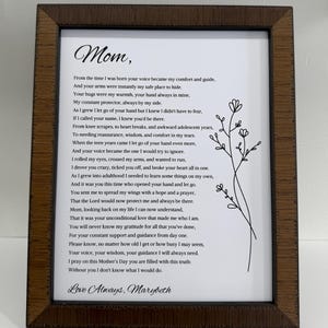 May include: A framed print with a heartfelt poem dedicated to "Mom." The text is in black script on a white background, accented by a delicate floral illustration. The frame is a dark brown wood, adding a classic touch.