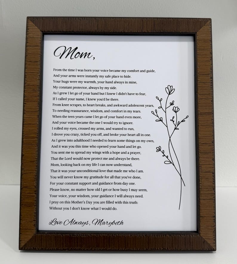 May include: A framed print with a heartfelt poem dedicated to "Mom." The text is in black script on a white background, accented by a delicate floral illustration. The frame is a dark brown wood, adding a classic touch.