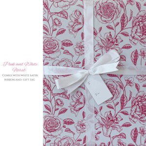 Pode incluir: Papel de embrulho floral rosa e branco com uma fita de cetim branca e uma etiqueta de presente. O papel de embrulho apresenta um padr&atilde;o repetido de rosas e outras flores rosa sobre um fundo claro.