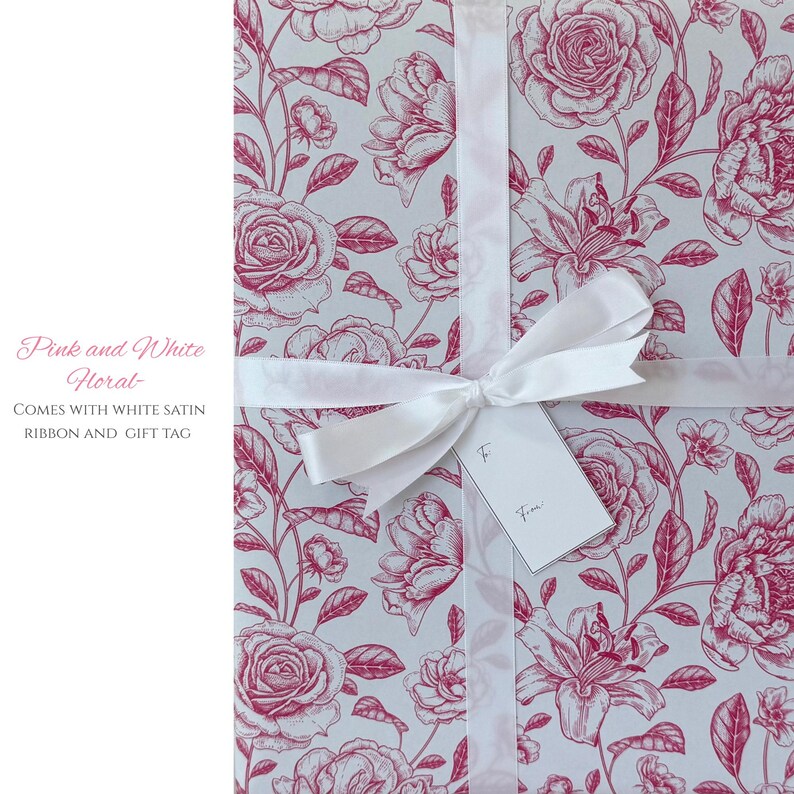 Pode incluir: Papel de embrulho floral rosa e branco com uma fita de cetim branca e uma etiqueta de presente. O papel de embrulho apresenta um padr&atilde;o repetido de rosas e outras flores rosa sobre um fundo claro.