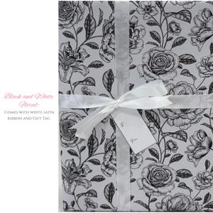 May include: Gift-wrapped package featuring a black and white floral pattern with roses and lilies. The package is tied with a white satin ribbon and includes a gift tag. The text on the package reads "Black and White Floral".