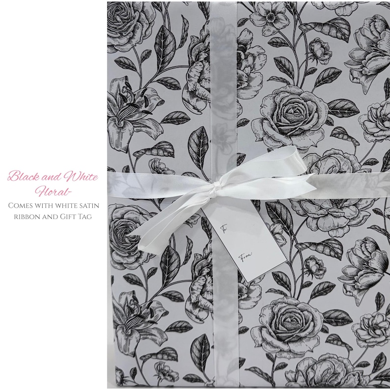 May include: Gift-wrapped package featuring a black and white floral pattern with roses and lilies. The package is tied with a white satin ribbon and includes a gift tag. The text on the package reads "Black and White Floral".