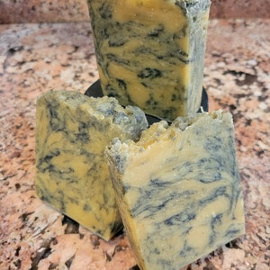 May include: Three bars of handmade soap with a marbled pattern of yellow and black. The soap is on a black surface.