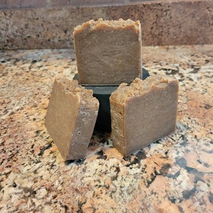 May include: Three brown bars of soap stacked on top of each other. The soap is a light brown color and has a rough texture.