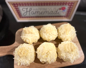 Può includere: Sei dolcetti rotondi, bianchi e dolci, ricoperti di cocco grattugiato su un tagliere di legno. Il tagliere ha un manico e il testo "Happiness is Homemade" è visibile sullo sfondo.
