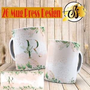 Puede incluir: Taza de cerámica blanca con diseño floral y la letra "R". La taza presenta hojas verdes, detalles dorados y un fondo estilo acuarela. El texto "26 Mug Press Design" está en la parte superior.