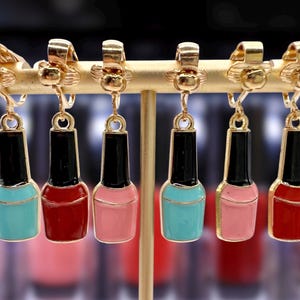 Könnte beinhalten: Sechs Paar goldene Ohrclips mit Nagellackflaschen-Anhängern. Die Anhänger sind in Türkis, Rot und Rosa.