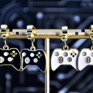 May include: A pair of black and white video game controller earrings. The earrings are hanging from gold-colored earring hooks.