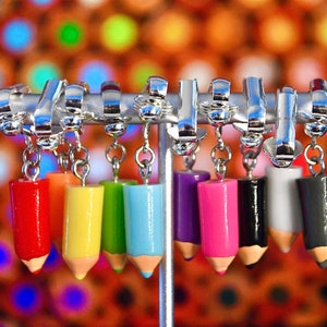 May include: A set of 8 colorful pencil earrings with silver hooks and chains. The pencils are red, yellow, green, blue, purple, pink, black, and gray.