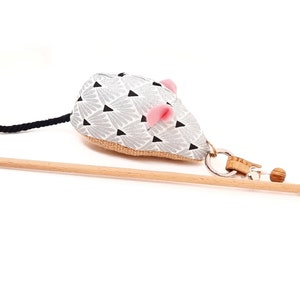 May include: A gray and black patterned cat toy mouse with pink ears attached to a wooden stick with a black and white string.