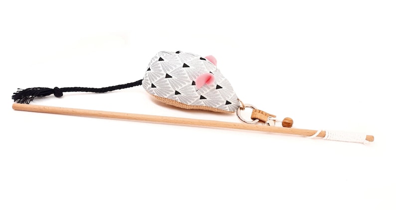 May include: A gray and black patterned cat toy mouse with pink ears attached to a wooden stick with a black and white string.
