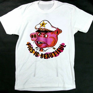 Puede incluir: Camiseta blanca con un cerdo rosa que lleva un sombrero de policía y el texto "PIGS IS BEAUTIFUL".
