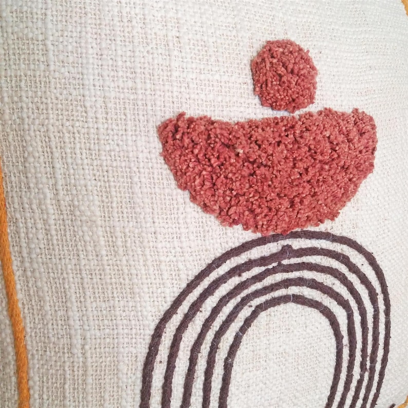 May include: A white throw pillow with a brown and red geometric design. The design features a circle, a half-circle, and a small circle.