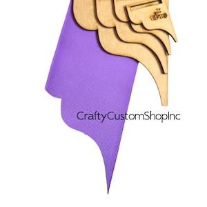 Op de afbeelding: Set van vier houten sjablonen voor het snijden van lint in verschillende maten. De sjablonen zijn op elkaar gelegd en hebben een gegolfde rand. De sjablonen liggen op een paars lint.