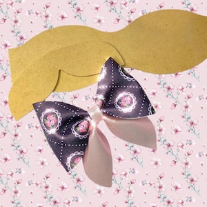 Puede incluir: Una plantilla de lazo de papel marrón con un lazo rosa y morado con un borde de encaje blanco y un patrón floral.