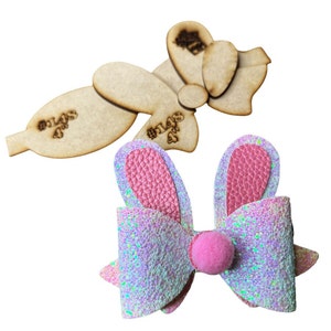 May include: A pink and white glitter bow with bunny ears. The bow has a pink pom-pom in the center. The bow is on a white background.