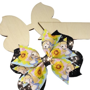 Puede incluir: Un lazo para el pelo azul y amarillo con un personaje de dibujos animados y girasoles. El lazo tiene un fondo de purpurina negro.