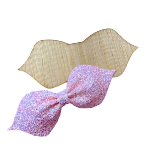 Puede incluir: Un lazo de purpurina rosa con un centro rosa claro. El lazo está sobre un fondo de madera.