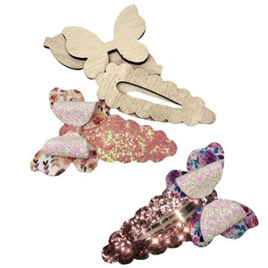 May include: Three wooden hair clips with glitter and floral patterns. The clips are shaped like butterflies and have a scalloped edge.