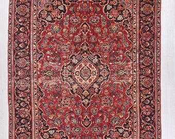 May include: A rectangular, antique Persian rug with a central red field and intricate floral patterns. The rug features a black border with floral motifs and a cream-colored central medallion. The design includes shades of red, black, cream, and touches of blue and green.