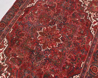 May include: A detailed, antique rug with a central floral medallion in shades of red, brown, and cream. The intricate pattern features geometric shapes and floral motifs, with a dark red border. The rug's design is symmetrical and ornate.