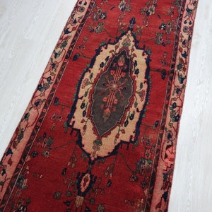 May include: A red runner rug with a traditional Persian design. The rug has a central medallion with intricate floral patterns and a border with repeating motifs.