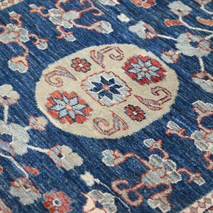 May include: A deep blue area rug featuring a central beige circular medallion with intricate floral and geometric patterns in shades of red, light blue, and white. The surrounding field displays repeating floral motifs in matching colors.