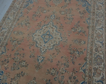 May include: A vintage rug with a peach-colored background and a central medallion with a blue and white design. The rug has a floral pattern throughout and a border with a blue and white design.