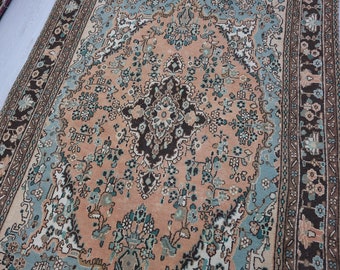May include: A vintage rug with a peach-colored background and intricate floral patterns in shades of blue, green, and brown. The rug has a border with a repeating design.