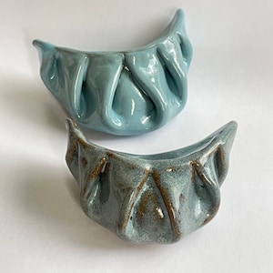 Peut inclure: Deux boulettes de c&eacute;ramique, l'une bleu clair et l'autre bleu fonc&eacute; avec des accents bruns. Les boulettes sont fa&ccedil;onn&eacute;es comme des boulettes chinoises traditionnelles.