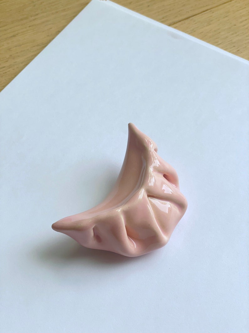 Peut inclure: Un plat en c&eacute;ramique rose en forme de ravioli. Le plat est verni et a une surface lisse et arrondie.