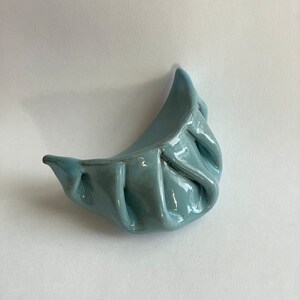 Peut inclure: Un plat en c&eacute;ramique de forme de ravioli de couleur bleu clair. Le plat est verni et a une finition lisse et brillante.