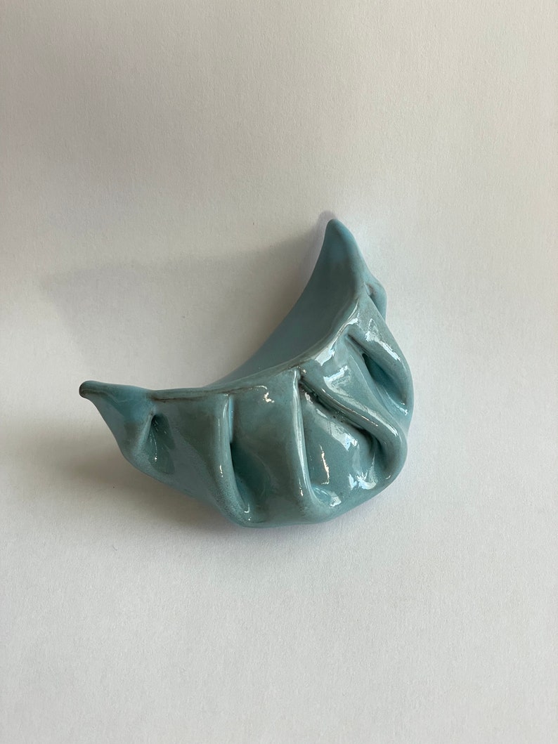Peut inclure: Un plat en c&eacute;ramique de forme de ravioli de couleur bleu clair. Le plat est verni et a une finition lisse et brillante.
