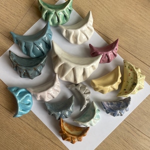 Peut inclure: Une collection de 15 raviolis en c&eacute;ramique de diff&eacute;rentes couleurs et motifs, notamment bleu, vert, jaune, marron et blanc. Les raviolis sont dispos&eacute;s sur une surface blanche.