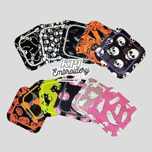 May include: A selection of square fabric items with Halloween designs. Patterns include skulls, skeletons, bats, spiders, pumpkins, black cats, and ghosts. The items are in black, orange, pink, and green. The text "KPI Embroidery" is visible.