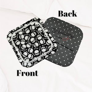 May include: Two square fabric items. One features a black and white skull and crossbones pattern, labelled "Front". The other, labelled "Back", is black with white polka dots and "KPI Embroidery" in script.