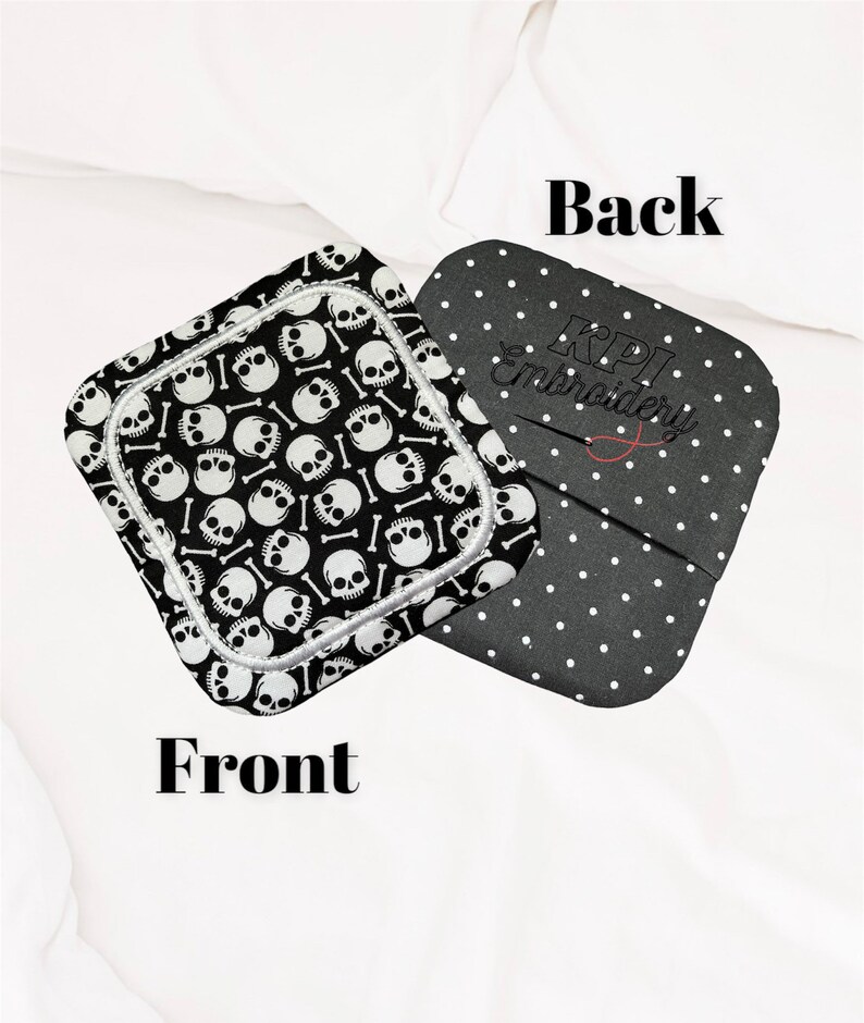 May include: Two square fabric items. One features a black and white skull and crossbones pattern, labelled "Front". The other, labelled "Back", is black with white polka dots and "KPI Embroidery" in script.