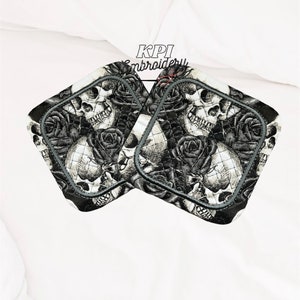May include: Two square pot holders featuring a black and white skull and rose design. The pot holders have a quilted pattern and a grey border. The text "KPI Embroidery" is visible at the top.