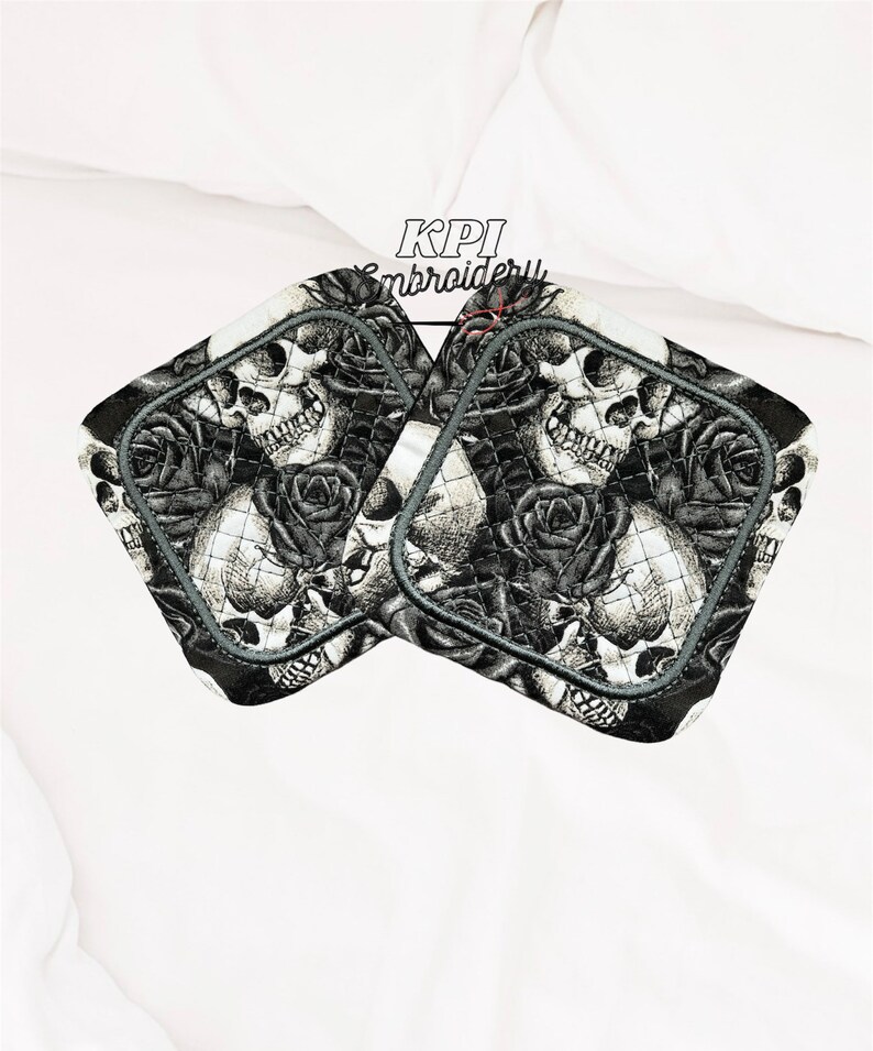 May include: Two square pot holders featuring a black and white skull and rose design. The pot holders have a quilted pattern and a grey border. The text "KPI Embroidery" is visible at the top.