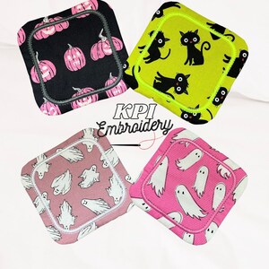 May include: Four square fabric coasters with Halloween designs. One has pink pumpkins on black, another black cats on lime green, and two show white ghosts on pink and mauve backgrounds. The coasters are square.