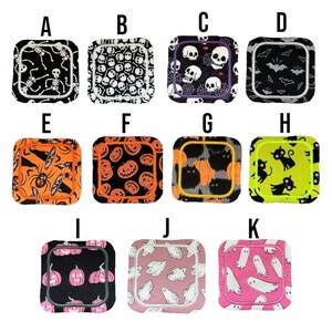 May include: A selection of square fabric coasters with Halloween designs. The coasters display patterns of skeletons, skulls, bats, spiders, pumpkins, and ghosts. They come in a range of colours, including black, orange, pink, and green.