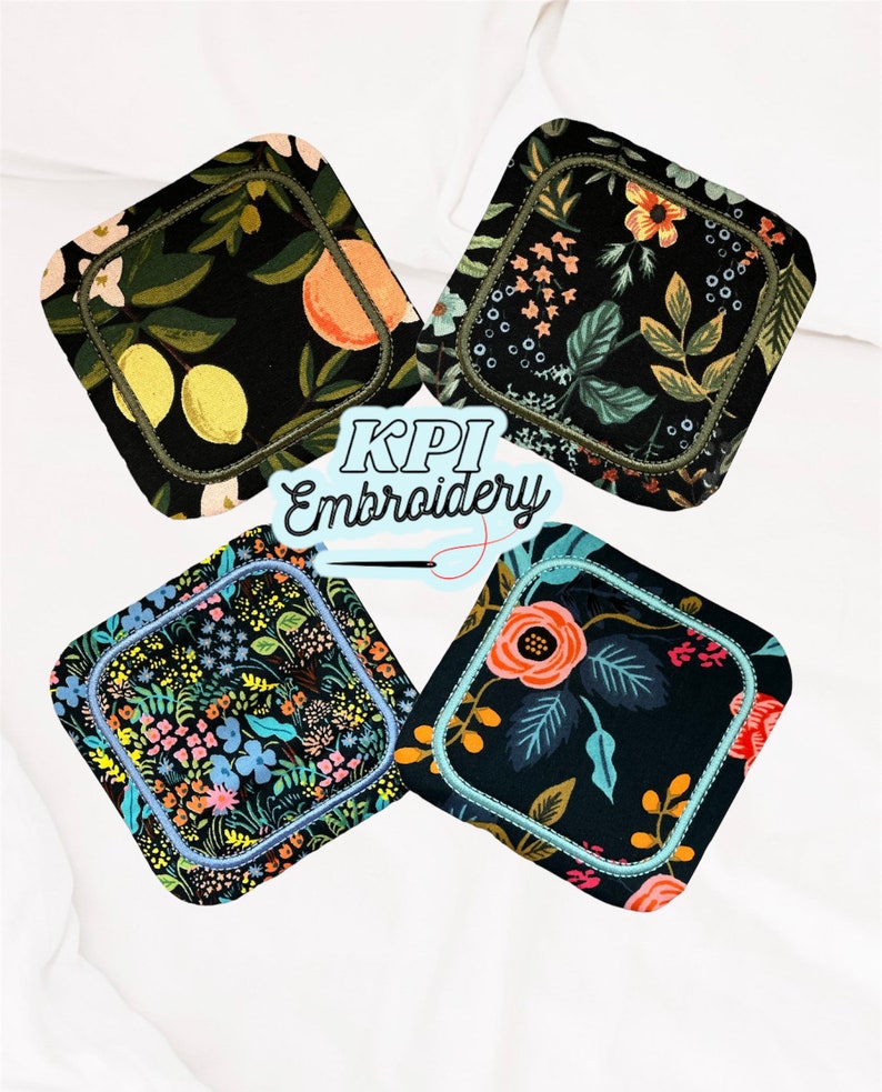 May include: Four square fabric coasters with rounded corners, each featuring a distinct black-based floral or fruit print. The coasters are outlined with decorative machine embroidery stitching. The text KPI Embroidery is centered in the image.