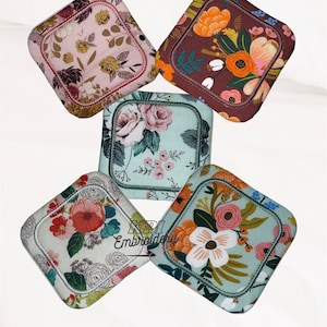 May include: Five square fabric coasters with rounded corners, each featuring distinct floral patterns in shades of pink, brown, orange, and light blue. The text KPI Embroidery is printed in black over the bottom left coaster.