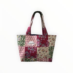 May include: A patchwork tote bag featuring a variety of floral and geometric patterns in shades of pink, green, cream, and red. The bag has two fabric handles and a white patch on the front with the text KPI Embroidery in a script font.