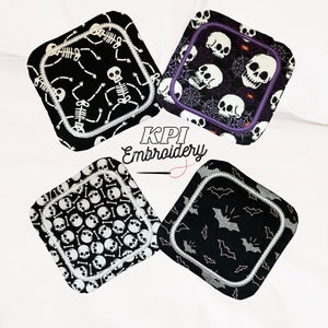 May include: Four square Halloween-themed coasters. Each coaster features a different black and white design: skeletons, skulls, skull pattern, and bats. The coasters have a white border and are from KPI Embroidery.