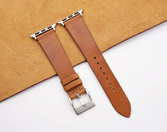 May include: Two brown leather watch straps with silver buckles. The straps are laid out on a brown suede surface.